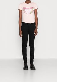 Camiseta rosa claro con un logotipo decorativo y un diseño colorido, combinada con jeans ajustados negros y zapatos negros con suelas gruesas y texturizadas.