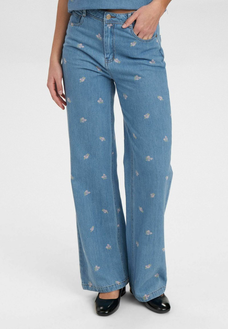 Lichtblauwe denim wijdemond spijkerbroek met een bloemenpatroon in pastelkleuren, voorzien van een standaard tailleband en zakken. Zwarte schoenen maken de look compleet.