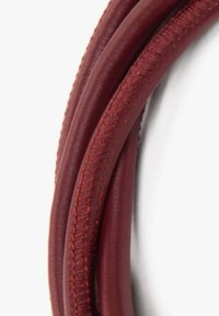 Červený kožený provaz s hladkým povrchem a mírně lesklým finišem, s kontrastním šitím podél okraje. Má zakřivený tvar.