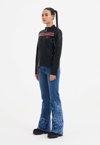 Sort zip-up jakke med rød og hvid striber; parret med blå flagrende jeans med indviklede blå mønstre ved kanten. Sorte platform sko.