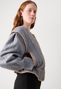 Gekwiltde grijze jas met oversized mouwen, beige accenten en een gestructureerd bloemenpatroon. Sluit met knopen en heeft een losse pasvorm.