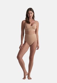 Nude lingerie set met een naadloze bralette met dunne bandjes en hoogzitende slips, beide van glad, zacht materiaal.