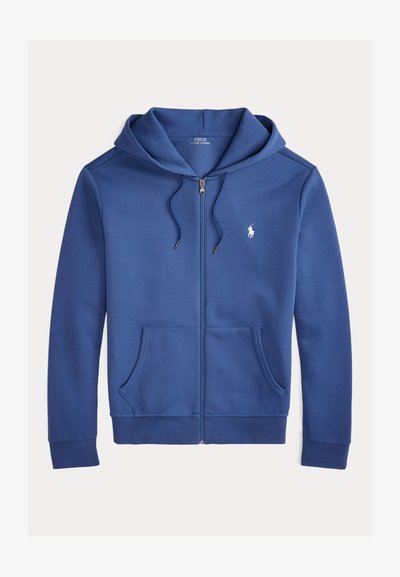 Tumši zila kapuce ar rāvējslēdzēju, izgatavota no mīksta materiāla, ar regulējamu kapuci, priekšējiem kabatām un mazu baltu logotipu uz krūtīm.