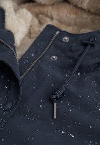 Wodoodporna granatowa kurtka z podszewką z futerka syntetycznego, wyposażona w zapinanie na zamek błyskawiczny, zatrzaski oraz kaptur ze ściągaczem i metalowymi detalami.