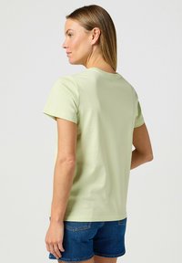 T-shirt verde chiaro a maniche corte con scollo rotondo, trama liscia e vestibilità casual, abbinato a pantaloni shorts in denim.
