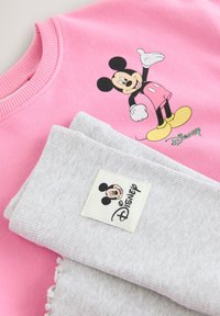Pink sweatshirt featuring a Mickey Mouse print with yellow shoes. A gray ribbed scarf with a Mickey label lies next to it.