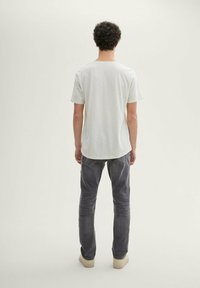 Light gray cotton t-shirt with short sleeves, round neckline, and a relaxed fit, paired with dark gray jeans and beige sneakers.