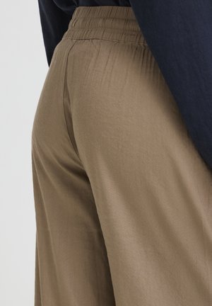 Primer plano de una persona con pantalones marrones de cintura elástica y una camiseta azul oscuro, mostrando la textura de la tela y los detalles de las costuras.