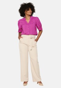 Blusa rosa brillante con maniche corte a sbuffo e bordi in pizzo; abbinata a pantaloni larghi a vita alta in crema e tacchi beige.
