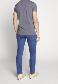 Grå kortärmad t-shirt, blå slim-fit jeans och gula canvas sneakers. Jeansarna har typisk kontrastsömnad och rak passform.