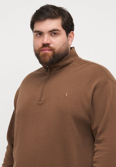Bruine ritssluiting pullover van zachte stof, met een hoge kraag en een geborduurd logo op de linkerborst. Eenvoudig ontwerp, ontspannen pasvorm.