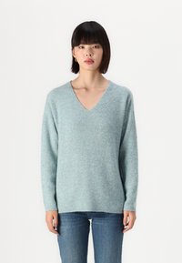 Sweater tricoté bleu clair avec un col en V, des manches longues, une coupe décontractée et une texture côtelée, associé à un jean bleu.