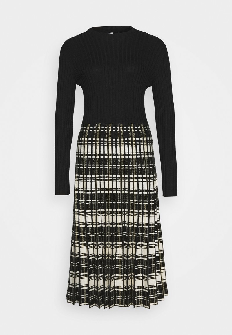 Robe noire à manches longues en maille côtelée avec une jupe plissée à motif à carreaux noir et blanc, longueur sous le genou.