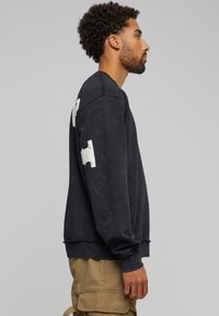 Zwarte sweatshirt met een zachte textuur, voorzien van witte grafische details op de mouwen en een relaxte pasvorm. Ribgebreide manchetten maken het ontwerp af.