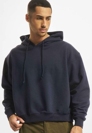 Marineblå bomulds hoodie med løs pasform, snøre til hætten og ribbede manchetter og bund. Glat tekstur uden synlige mønstre eller detaljer.