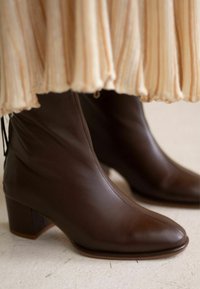 Brown leather ankle boots with a pointed toe and block heel. The upper has a smooth texture, with subtle gathering near the top.