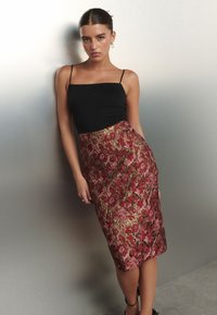 Crni uski top na bretele uparan s cvjetnom bordo suknjom s detaljima u zlatu. Glatka tekstura, do koljena, s bočnim džepovima.