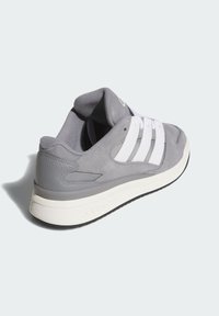 Gray suede sneaker with white fabric stripes, padded collar, and a rubber sole. Features smooth and textured materials.