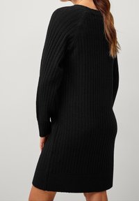 Robe pull noire côtelée à manches longues, col rond, longueur genoux, en tissu texturé, avec une coupe ajustée.