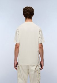 Μπεζ κοντομάνικο μπλουζάκι από βαμ�βάκι, με λαιμόκοψη crew και καθαρό, μινιμαλιστικό σχέδιο, συνδυασμένο με ανοιχτό μπεζ παντελόνια cargo.