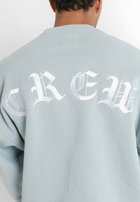 Felpa azzurro chiaro con grande lettering gotico bianco che scrive "CREW" sul retro. Realizzata in tessuto morbido, con una vestibilità confortevole.