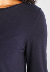 Maglione blu navy con maniche lunghe, scollo rotondo e texture a coste. Il materiale sembra morbido e leggermente elasticizzato.