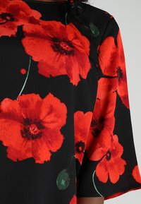 Top noir avec imprimé de grandes coquelicots rouges, manches courtes et accents verts. Texture lisse avec un design fluide.