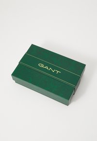 Gr�üne Geschenkbox mit Muster und goldfarbenem "GANT"-Logo auf der Vorderseite. Verfügt über eine strukturierte Oberfläche und ein einfaches Falt-Design.