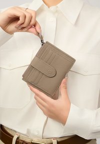 Taupe leren portemonnee met gestructureerd oppervlak, voorzien van een flapafsluiting, meerdere kaartsleuven en een ritsvak, gehouden in een hand.