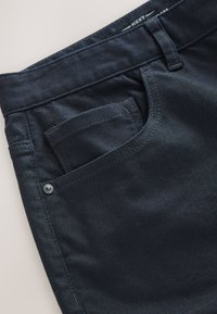 Marineblå denimbukser med frontlomme og kontrastsyning, med en glat tekstur og minimalistisk design.