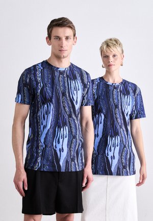 Short-sleeve t-shirts in blue with abstract patterns, featuring a crew neckline and a blend of dark and light hues. Models wear casual bottoms.