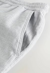 Pantalons en tissu gris clair avec un waistband élastique et un gros plan sur la couture d'une poche latérale.