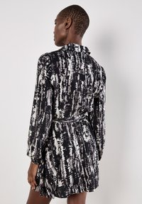 Vestido de manga corta en tejido estampado en blanco y negro, con cintura ceñida por un cinturón y cuello, que presenta una falda fluida y un diseño texturizado.