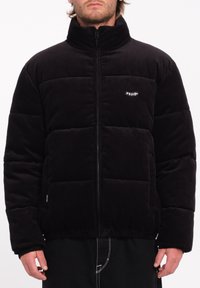 Schwarze Cordura-Puffjacke mit hohem Kragen, Reißverschluss und horizontaler Steppung. Verfügt über ein Logo-Patch und einen elastischen Bund.