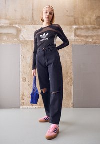 Svart genomskinlig långärmad topp med vitt Adidas-logotyp, kombinerad med svart högmidjade jeans med trasiga knän och rosa Adidas-skor. Blå väska.