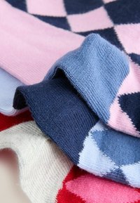 Tessuto lavorato a maglia multicolore con grandi motivi a rombo in blu navy, rosa, azzurro, crema e rosso. Texture morbida, bordi ripiegati.