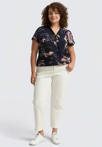 Blusa blu navy a maniche corte con stampa floreale, vestibilità comoda, abbinata a pantaloni corti avorio e sneakers bianche. Tessuto liscio, chiusura con bottoni.