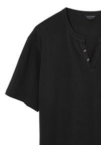 T-shirt nero a maniche corte con scollatura henley, caratterizzato da tre bottoni decorativi e un tessuto di cotone strutturato. L'etichetta mostra "Calliope" e taglia "L."