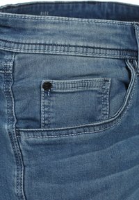 Jeans denimowe w lekko wybledzonym niebieskim kolorze, z pięcioma kieszeniami oraz widocznymi detalami przeszycia na pasku i tylnej kieszeni.