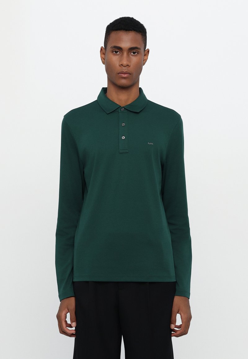 Grønn langermet polo skjorte laget av myk stoff, med krage, plakk med tre knapper og en liten logo på venstre bryst.