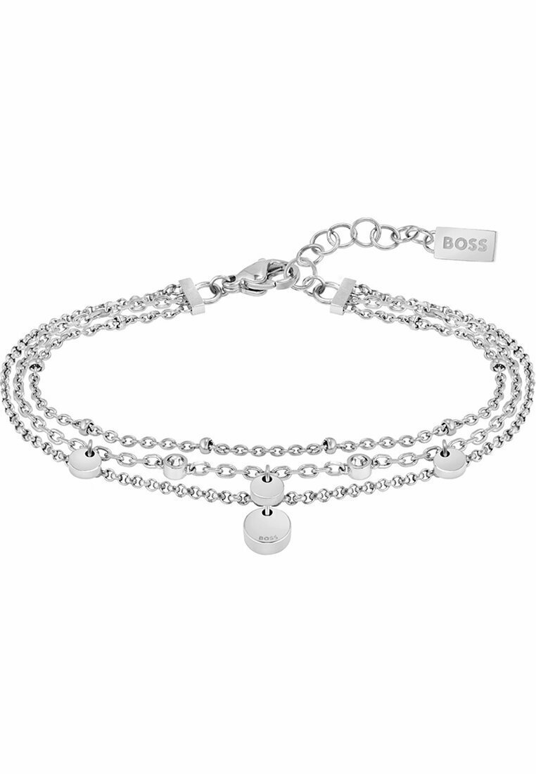 Sølvfarget armbånd med tre lagdelte kjeder. Har runde metalliske detaljer og en karabinlås med et merke som viser merkevaren.