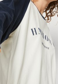 Weißes und marinefarbenes Langarmshirt mit lockerem Schnitt. Auf der Vorderseite befindet sich ein grafischer Druck mit dem Wort "HARMONY". Hergestellt aus Baumwolle mit weicher Textur.
