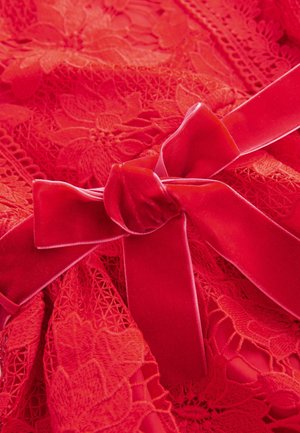 Roter Spitzenstoff zeigt florale Muster, detaillierte Nähte und ein Samtbogen, akzentuiert durch eine glatte Textur und lebendige Farbe.