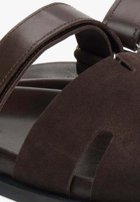 Brown sandal featuring suede upper and leather straps, open-toe design with cutouts, and a smooth black sole.