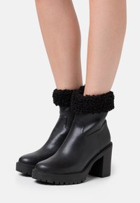 Schwarze Lederstiefeletten mit einer strukturierten, schwarzen Fleeceumschlag, einem klobigen Absatz und einer Gummisohle mit einem Profildesign.