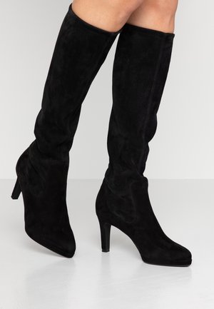 Black suede knee-high boots with rounded toes and medium high heels worn on bare legs against a light background.