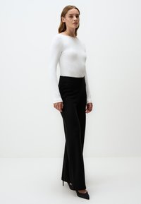 Haut blanc à manches longues avec une texture lisse, associé à un pantalon noir taille haute, présentant une coupe ajustée et des jambes évasées.