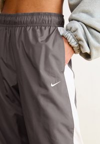 Nike pilki sportiniai kelnių su baltais šonų akcentais, elastingu juosmeniu ir kišenėmis. Minkšta, lygi tekstūra, su mažu siuvinėtu logotipu.