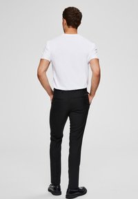 Pantalons noirs slim, avec poches arrière. Assortis à un t-shirt blanc à manches courtes. Tissu lisse avec un léger éclat.
