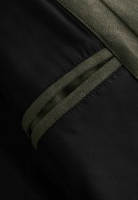 Black fabric with a smooth texture alongside dark green suede accents. Features stitched seams and a visible pocket detail.